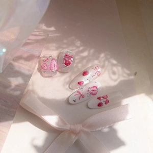 Close-up of pink strawberry themed press-on nails with ribbon bows and silver stars