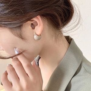 Vintage C-shaped beige glossy hoop earrings worn by a model in a side profile shot