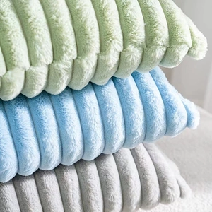 Close-up of stacked faux rabbit fur pillows with wavy texture in green, blue and grey
