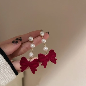 Macro detail of red velvet bow earrings with elegant white pearl beads and gold accents