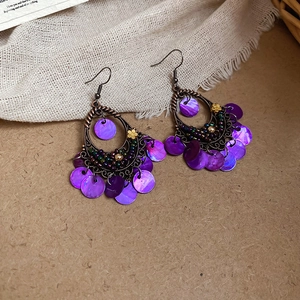 Detail of bohemian fish-shaped shell tassel earrings with purple sequins and bronze hooks