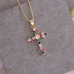 Detail of 18K gold cross pendant necklace with colorful cubic zirconia on stone surface