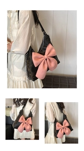 Detail showing the large pink bow design and silver metal chain on a black leather bag