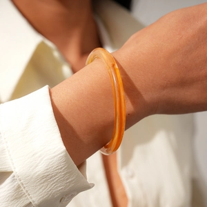 Close-up of translucent amber acrylic bangle with glossy finish on a wrist