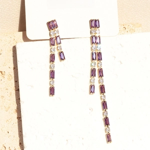Detailed view of long gold tassel earrings with purple crystals and zircons on card