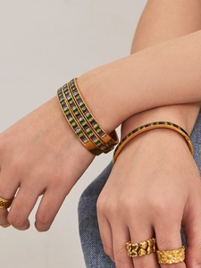 Close-up of stacked gold bangles with colorful zircon stones and matching rings