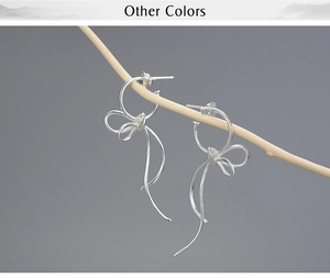 Macro detail of silver S925 bow tassel earrings hanging on a rustic wooden branch