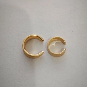 Macro shot of two polished gold-tone metal ear cuffs with a glossy finish on white surface