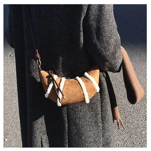 Detail einer braunen Wildleder-Croissant-Tasche mit weißem Kunstfellbesatz und Knotengurt