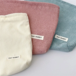 Detailed corduroy texture of makeup bags in cream, pink and blue with woven labels