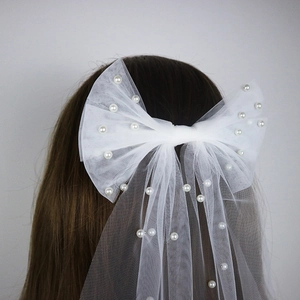 Detail of white mesh bow hair clip with faux pearls worn by a bride for a wedding