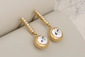 Detailed view of gold tassel earrings with sparkling crystals on a geometric display
