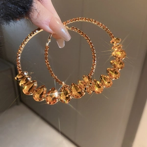 Détail de grandes créoles dorées ornées de cristaux de couleur champagne en poire