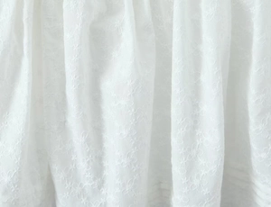 Detailansicht von weißem Kleiderstoff mit Blumenstickerei und elegantem Faltenwurf der Textur