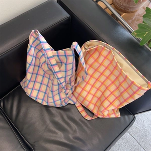 Detail of plaid canvas bags with knotted straps and zippers on a leather sofa