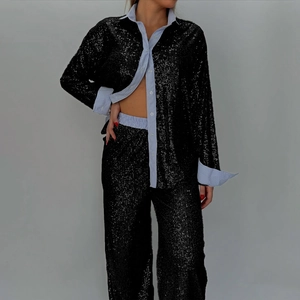 Detail shot of shimmering black sequin fabric texture on luxury two-piece shirt and pants set