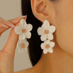 Détail de boucles d'oreilles élégantes à double fleur blanche avec centre doré sur un mannequin