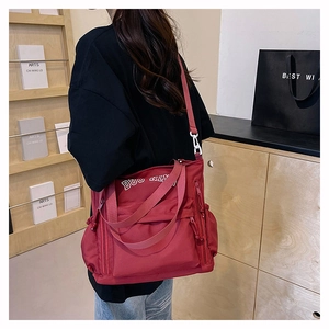 Close-up of the red canvas tote bag showing wide shoulder strap and side zipper detail