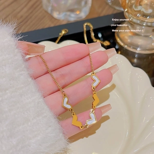 Close-up of heart-shaped gold necklace with white shell inlay held in hand for detail