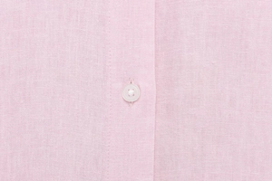 Close-up of pink linen fabric texture with a transparent four-hole button on the shirt