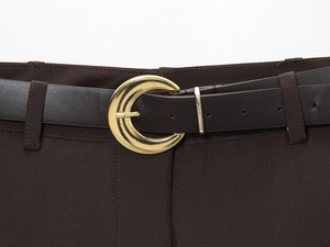 Détail d'une ceinture en cuir marron foncé avec boucle métallique dorée en forme de croissant