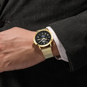 Business men's watch with gold mesh band and black Roman numeral dial worn on wrist