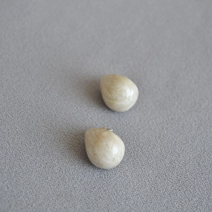 Close-up of teardrop enamel earrings with cream marble texture and gold plating details