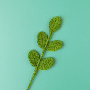 Handmade crochet green leaf sprig with five leaves on a solid minimalist background