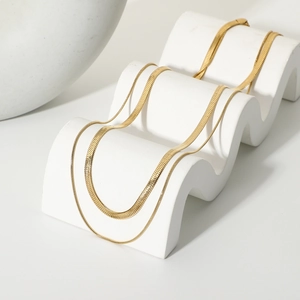 Detail view of a double-layered gold snake chain necklace on a white display stand