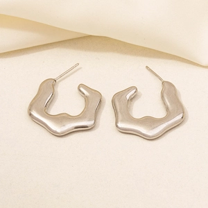 Macro shot of silver irregular geometric earrings on soft beige fabric background