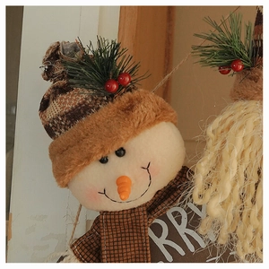 Close-up of a plush snowman ornament featuring a plaid hat, carrot nose, and Merry text