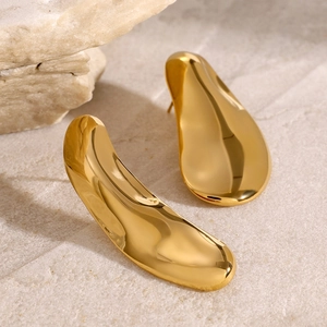 Macro detail of abstract organic gold earrings in 18k stainless steel on beige stone