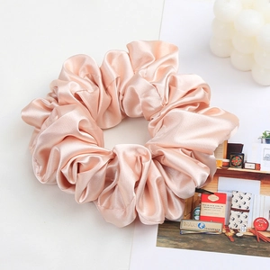 Detailed texture of a soft pink satin scrunchie with silk sheen and pleated design