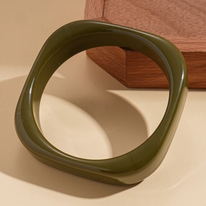 Detail of olive green resin geometric bangle with wave texture on a beige background