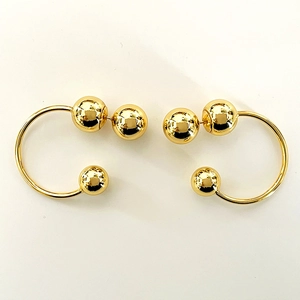 Detailed close-up of golden C-shaped hoop earrings with three polished metallic spheres