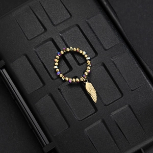 Detail of beaded ring with golden beads and iridescent charms featuring a gold feather pendant