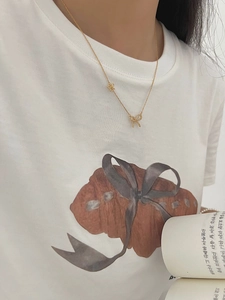 Detail shot of a layered gold bow pendant necklace on a delicate chain worn by a model