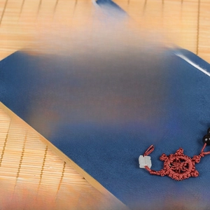 Macro detail of 108 ebony wood prayer beads with a red knot on a blue board