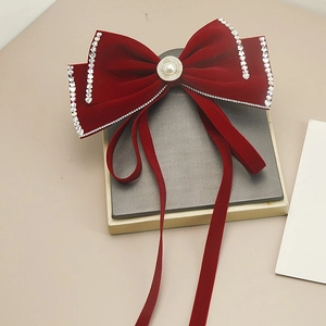 Dettaglio del fermaglio con fiocco in velluto rosso, strass brillanti e grande perla