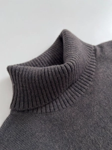 Detailed close-up of dark grey ribbed turtleneck collar on a soft knit sweater