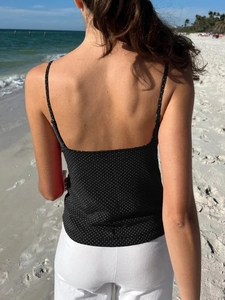 Outdoor beach lifestyle shot showing the back of a black polka dot camisole crop top
