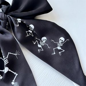 Silk hair scrunchie with long bow ribbon featuring white skull print on black fabric