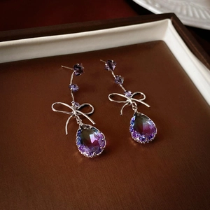 Detail of silver bow earrings with gradient purple teardrop crystals on leather