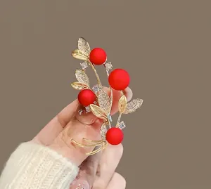 Elegant red berry brooch with golden leaves and sparkling crystals on a knit sweater