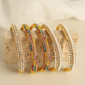 Luxurious matte gold open bracelets with colorful crystals and pearls on rock decor