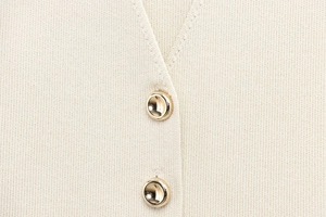Détail d'un gilet en maille beige avec boutons en métal doré poli et maille fine