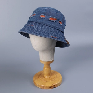 Distressed blue denim bucket hat with orange ripped details on a display stand