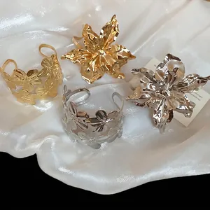 Exaggerated metal flower bangles in gold and silver plating on white satin background