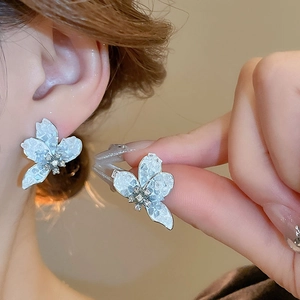 Macro shot of silver flower earrings with light blue petals and sparkling white rhinestones