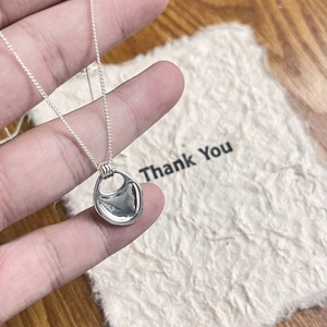 Minimalist silver saddle pendant necklace on fine O-chain held by hand against a card